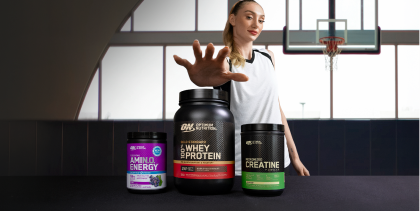 Cam Brink holding out hand towards Optimum Nutrition protein products on a table.
