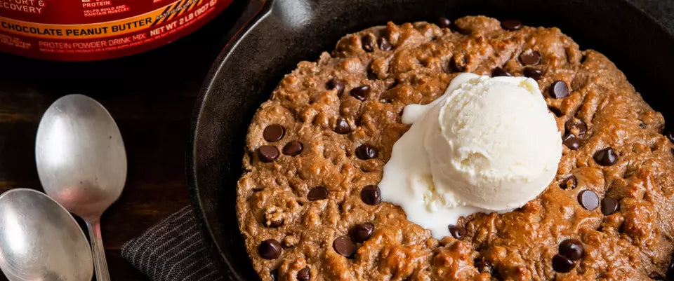 Skillet cookie topped with ice cream, next to a container of protein peanut butter powder