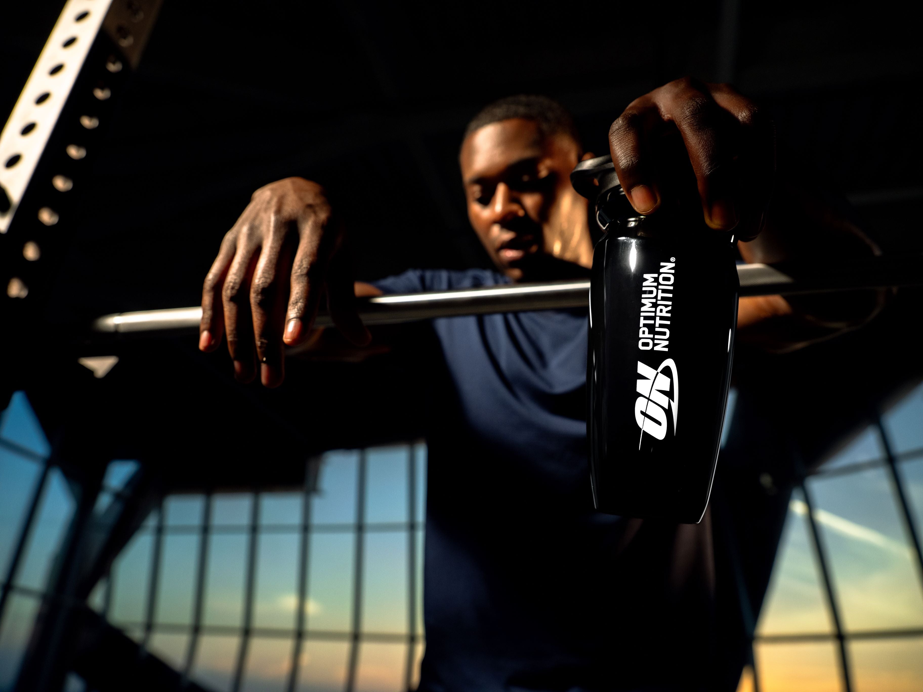 Person holding a black shaker bottle with 'Optimum Nutrition' branding against a dark background.