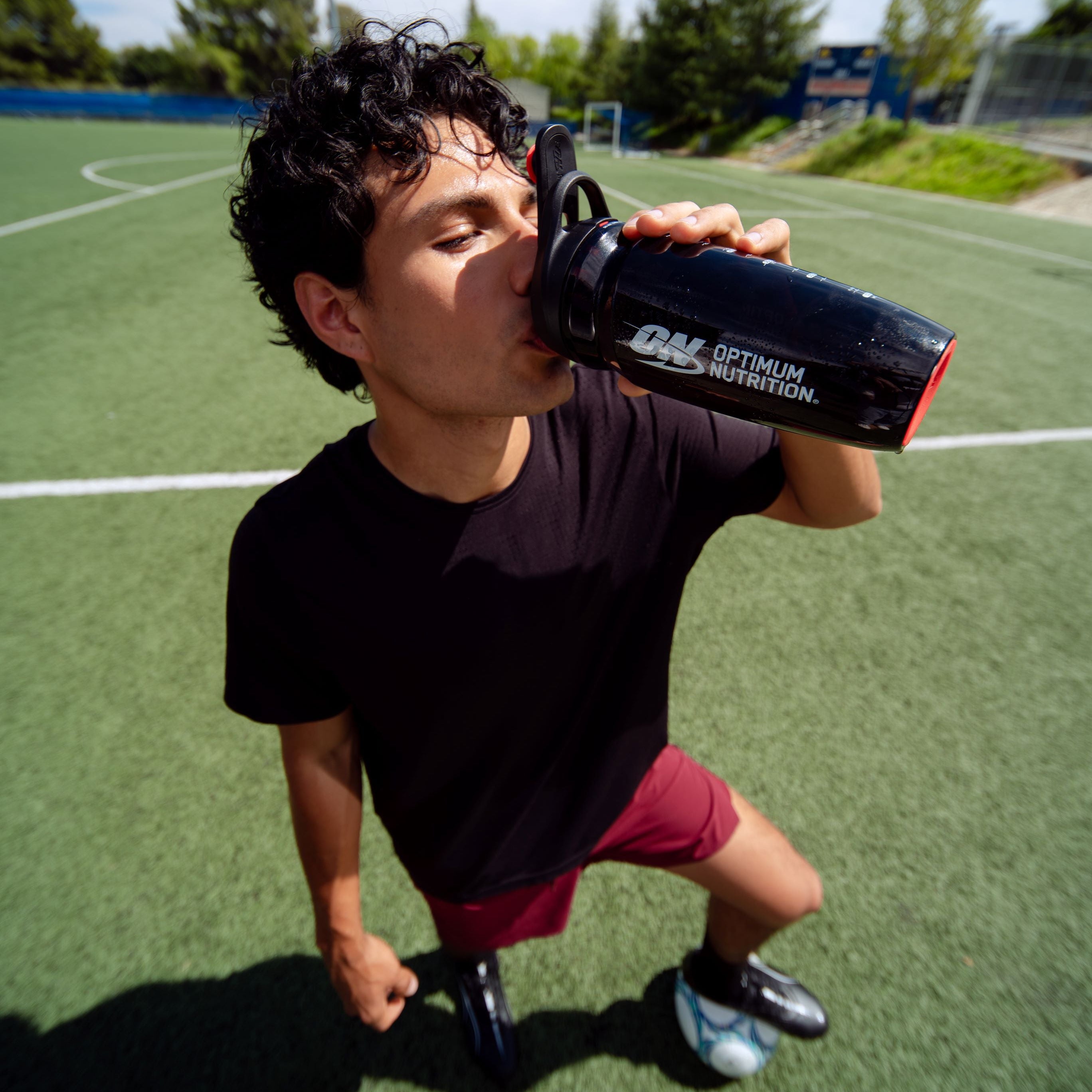 Person drinking from a water bottle on a sports field