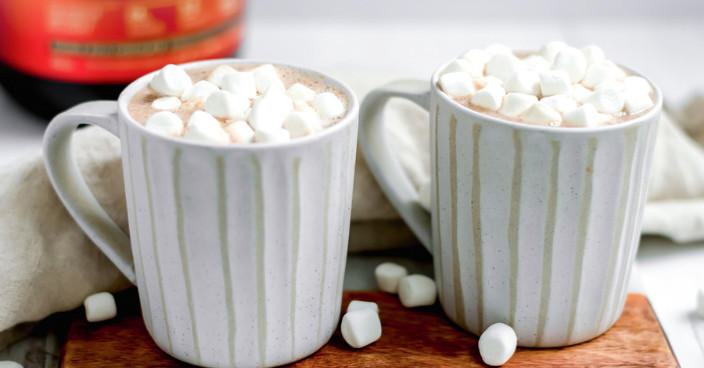 Two mugs filled with hot chocolate topped with marshmallows, placed on a wooden surface